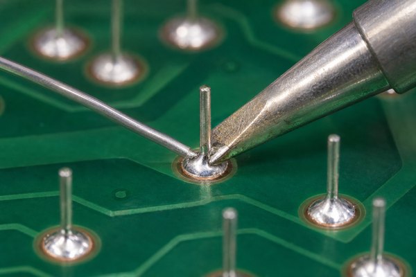 Soldering iron heating a PCB pad and component lead while solder is fed into the joint